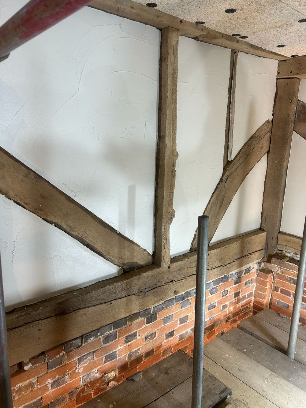 Oak timber-framed wall with freshly applied lime plaster panels above a brick plinth